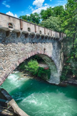 Steinerner Steg köprüsünün her iki tarafında yemyeşil ağaçlar olan bir nehri geçerken görüntüsü, Merano, Güney Tyrol, İtalya 'da ikonik bir simge.