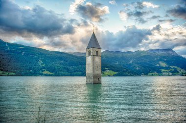 The iconic old church Tower of Graun emerging from the water of the artificial lake of Reschensee in Curon Venosta, South Tyrol, Italy clipart