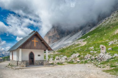 Arka planda Tre Cime di Lavaredo 'nun zirveleri olan bir dağ geçidinde küçük bir kilise duruyor.