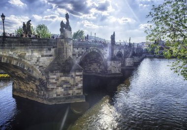 PRAGUE - 10 Mayıs 2024: Prag 'daki Charles Köprüsü' nde Prag Kalesi ve Vltava nehri üzerinde güneşli yaz gününde yürüyen turistler