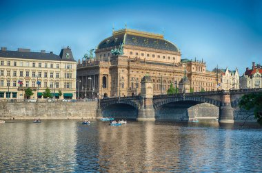 Prag 'daki Vltava nehrinin kıyısında oturan Ulusal Tiyatro, güneşli bir günde kürek çeken turistlerle birlikte.