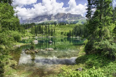 Carezza Gölü 'nün zümrüt yeşili suları, güneşli bir yaz gününde İtalyan Dolomitleri, Trentino Alto Adige, İtalya' daki Rosengarten grup dağlarının tepelerini yansıtır.
