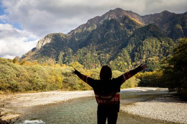 Orta Kamikochi Milli Parkı 'nın güzel bir arka planına sahip Asyalı kız. Kar yamacı, kaya ve Azusa nehri. Sonbahar mevsiminde yaprak değiştirme renginde tepe örtüsü..