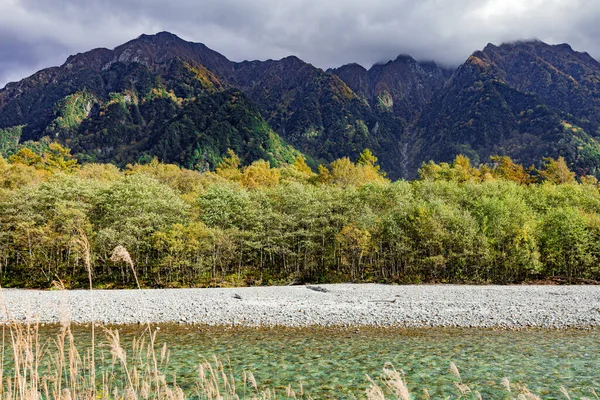 Kamikochi\'s hiking trail that walks through a nature trail in the heart of the Japanese mountains with the beauty of pines and mature trees changing their colors in the fall.