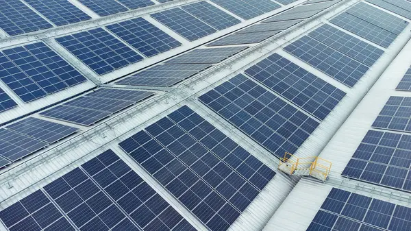 Bir binanın çatısına birden fazla güneş paneli yerleştirildi. Güneş panelleri düzenli sıra ve sütunlar halinde düzenlenir, her panel arasında net ayrılıklar bulunur. 