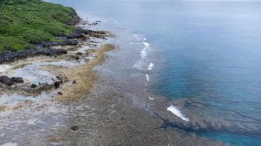 Okinawa 'da deniz yüzeyi temiz su ve insansız hava aracının öfke bakışından kayayla kaplı..