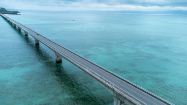 Okinawa, Japonya - Temmuz 2024: Kouri Adası 'nın uzun köprüsü ve açık gökyüzü ve deniz suyuna sahip insansız hava aracı tarafından yüksek görüş alanından kumsal.