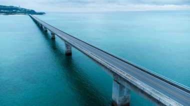 Okinawa, Japonya - Temmuz 2024: Kouri Adası 'nın uzun köprüsü ve açık gökyüzü ve deniz suyuna sahip insansız hava aracı tarafından yüksek görüş alanından kumsal.