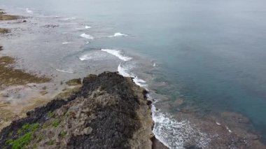 4K Okinawa 'nın sakin deniz manzarası kristal berrak suları, açıkta kayalık oluşumlar ve kıyıya vuran nazik dalgalar sergiliyor.