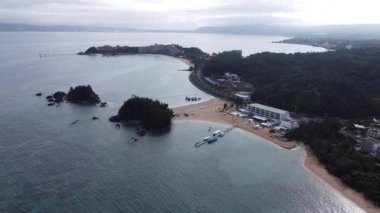 4K Okinawa 'nın sakin deniz manzarası üzerinde kristal berrak sular, açıkta kayalık oluşumlar ve kıyıya doğru hafif dalgalar.