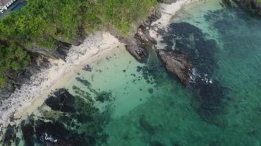 4K Okinawa 'nın sakin deniz manzarası üzerinde kristal berrak sular, açıkta kayalık oluşumlar ve kıyıya doğru hafif dalgalar.