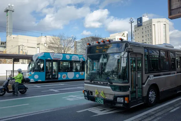 Okayama Şehri, Japonya - Aralık 2024: Merkezi ulaşım merkezi Okayama İstasyonu 'nun önündeki kentsel alanın geniş görünümü. Sahnede sakin binalar, yerel otobüsler, tramvaylar ve yayalar yer alıyor..