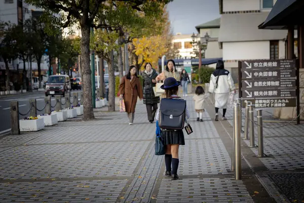 Japonya - Aralık 2024: Genç üniformalı Japon öğrenci okuldan sonra, geleneksel bir Randoseru sırt çantası taşıyarak tek başına kaldırımda yürüyor. Sahne Japonya 'daki günlük hayatın bir anını yakalar.