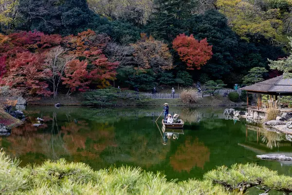 Kagawa, Japonya - Aralık 2024: Sonbahar sezonu boyunca Takamatsu 'daki Ritsurin Park' ın nefes kesici manzarası. Kırmızı ve turuncu renkli akçaağaç ağaçlarıyla geleneksel Japon bahçesi, sakin yansıtıcı havuzlar.