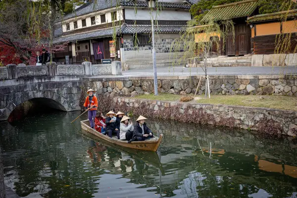 Okayama Bölgesi, Japonya - Aralık 2024: Canlı sonbahar sezonu boyunca Kurashiki Bikan Tarihi Çeyreği manzarası. Turistler geleneksel beyaz duvarlı binalar, akçaağaç ağaçları ve kanallarla dolu korunmuş Edo dönemi caddeleri boyunca yürüyorlar.