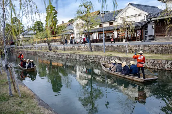 Okayama Bölgesi, Japonya - Aralık 2024: Canlı sonbahar sezonu boyunca Kurashiki Bikan Tarihi Çeyreği manzarası. Turistler geleneksel beyaz duvarlı binalar, akçaağaç ağaçları ve kanallarla dolu korunmuş Edo dönemi caddeleri boyunca yürüyorlar.