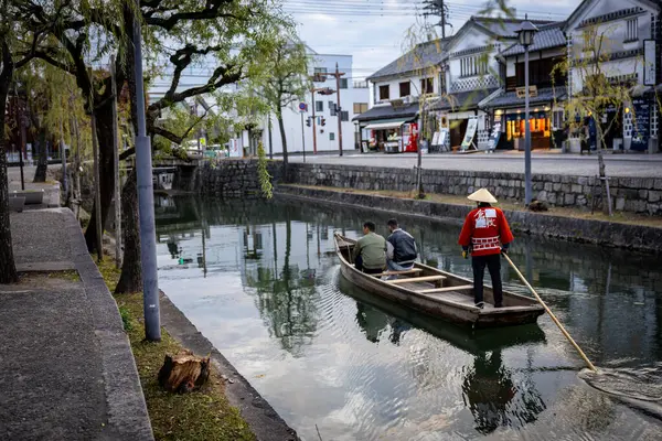 Okayama Bölgesi, Japonya - Aralık 2024: Canlı sonbahar sezonu boyunca Kurashiki Bikan Tarihi Çeyreği manzarası. Turistler geleneksel beyaz duvarlı binalar, akçaağaç ağaçları ve kanallarla dolu korunmuş Edo dönemi caddeleri boyunca yürüyorlar.