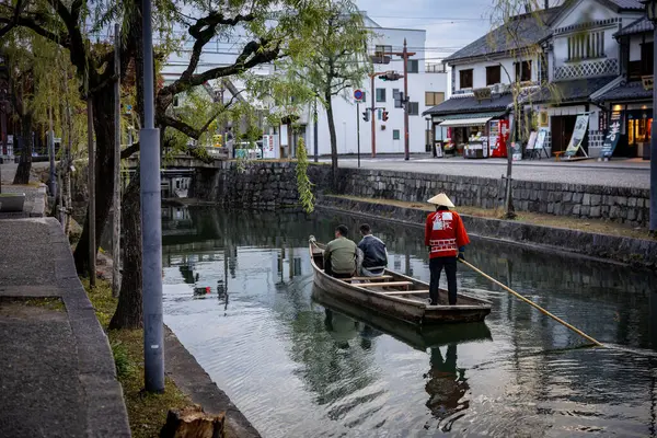 Okayama Bölgesi, Japonya - Aralık 2024: Canlı sonbahar sezonu boyunca Kurashiki Bikan Tarihi Çeyreği manzarası. Turistler geleneksel beyaz duvarlı binalar, akçaağaç ağaçları ve kanallarla dolu korunmuş Edo dönemi caddeleri boyunca yürüyorlar.