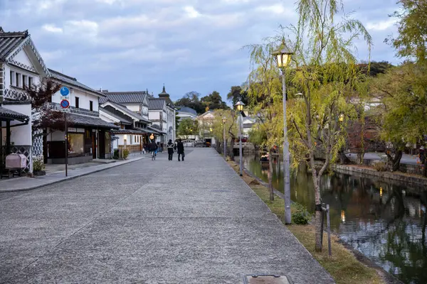 Okayama Bölgesi, Japonya - Aralık 2024: Canlı sonbahar sezonu boyunca Kurashiki Bikan Tarihi Çeyreği manzarası. Turistler geleneksel beyaz duvarlı binalar, akçaağaç ağaçları ve kanallarla dolu korunmuş Edo dönemi caddeleri boyunca yürüyorlar.