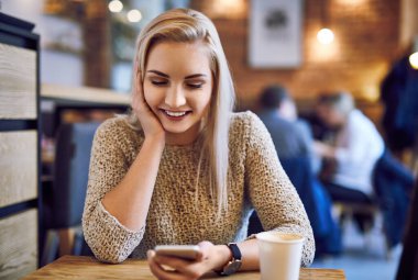 Bir kafede akıllı telefonunu kullanan güzel genç bir kadın.