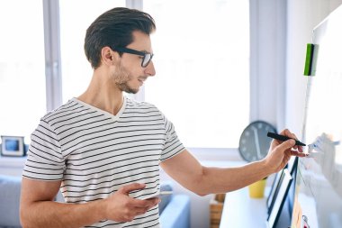 Küçük ofisteki beyaz tahtaya fikirler yazan genç web geliştiricisi