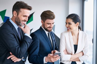 Ofiste kahve molası sırasında konuşan bir grup işletme yöneticisi akıllı telefondan bir şey paylaşıyor.