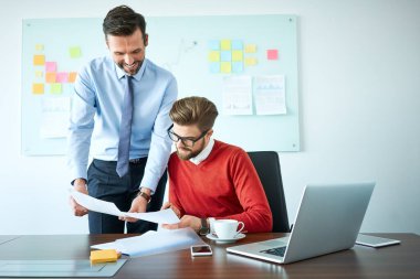 İki iş arkadaşı ofiste görüşüyor, belgeler ve planlama stratejisi gösteriyor.