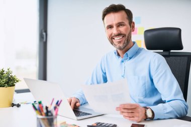 Ofiste dizüstü bilgisayarla çalışan mutlu iş adamı