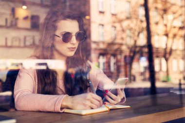 Kafedeki kadın akıllı telefon kullanıyor ve not alıyor.