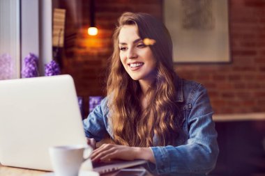 Kafede dizüstü bilgisayarını kullanan güzel genç bir kadın.