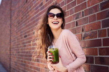 Mutlu kadın ıspanaklı smoothie içiyor, sokaklarda gülümsüyor.