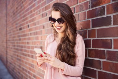 Şehir caddesinde telefonuyla mesajlaşan mutlu genç bir kadın.