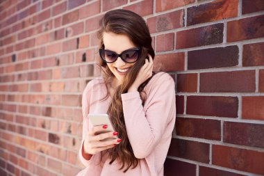 Akıllı telefonundan mesaj okuyan gülümseyen genç bir kadın.