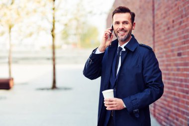 Kendine güveni tam bir iş adamı dışarıda kahve içerken telefonda konuşuyor.