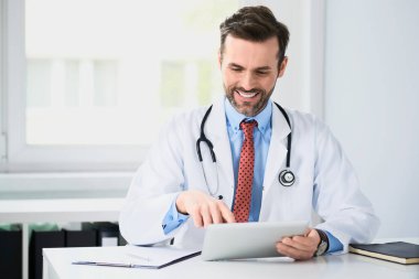 Mutlu doktor masada oturuyor, tablet kullanıyor.