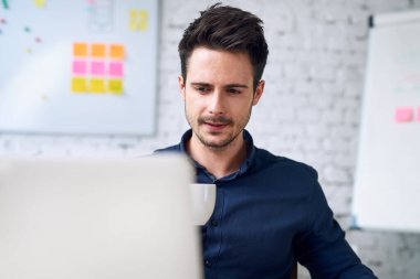 Kahve içip dizüstü bilgisayara bakan yakışıklı iş adamının portresi.