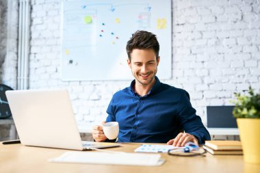 Genç girişimci iş adamı kahve içiyor ve bilgisayarla ve belgelerle çalışıyor.