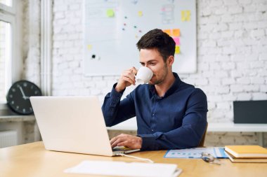 Kahve içen ve ofis bilgisayarını kullanan yakışıklı bir iş adamı.