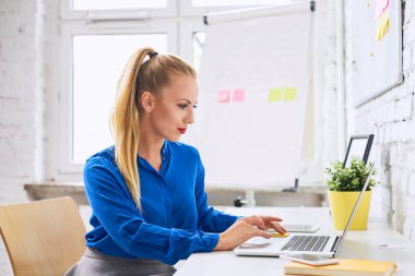 Alternatif modern ofiste dizüstü bilgisayarda çalışan güzel, kendine güvenen genç bir kadın.