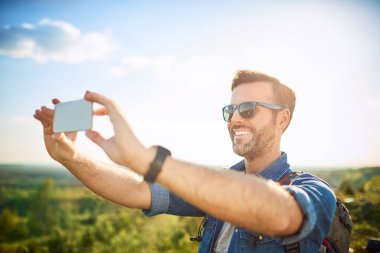 Dağlarda yürüyüş yaparken selfie çeken mutlu bir adam.
