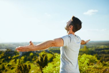 Kollarını açıp güneşli bir günde ormanın manzarasına hayran olan bir adam.