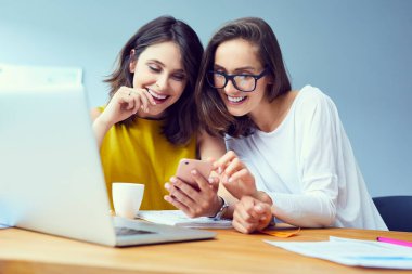 Ofisteki iş molasında telefon kullanan ve gülen güzel genç ofis çalışanları.