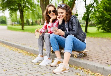 Parkta uzun panoda oturan kadın çift akıllı telefona bakıyor.