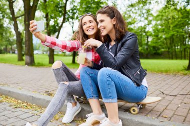 Arkadaşlık - Mutlu genç kadınlar parkta birlikte oturup selfie çekiyorlar