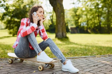 Güzel, genç bir kadın, uzun bir tahtanın üzerinde otururken telefonda konuşuyor.
