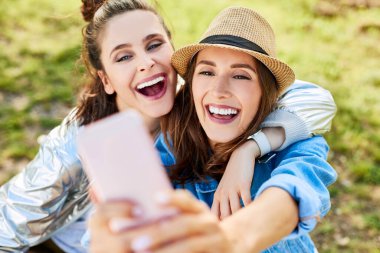 İki genç kadın birbirlerine sarılırken selfie çekiyorlar.