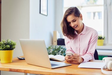 Evde çalışan genç bir kadın cep telefonuyla mesajlaşıyor. 