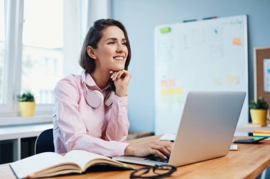 Ofiste laptopuyla çalışan ve gülümseyen genç bir kadın.