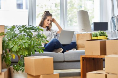 Yeni daireye taşınırken dizüstü bilgisayar kullanan genç bir kadın.