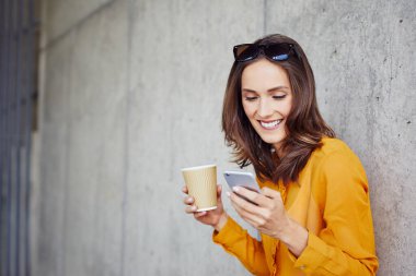 Telefonu kullanan ve kahve içen çekici genç bir kadının portresi.